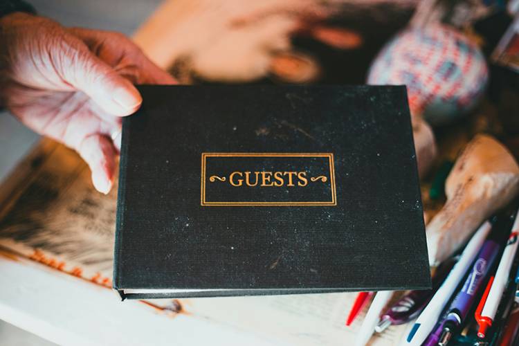 Hand holds black album with gold lettering that says "Guest Book"