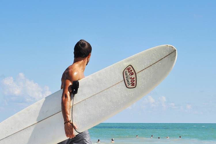 Man stands on beach holding surfboard.